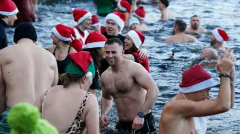 PA Media Image shows swimmers in their bathing suits and Christmas hats attending a Christmas Day dip in Blackroot Pool, Sutton Park, in Sutton Coldfield, Birmingham on 25 December, 2025