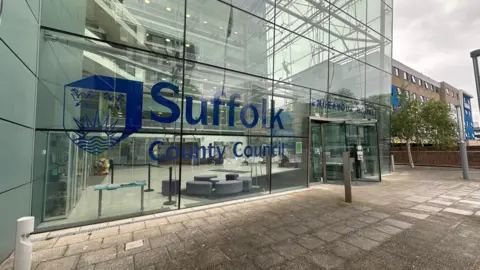 Alice Cunningham/BBC The front of Endeavour House, the headquarters of Suffolk County Council, which is written in large blue letters across the glass front of the building.