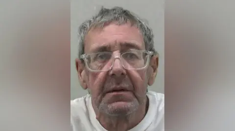 Northumbria Police Mugshot of an older man with grey hair and clear-rim glasses