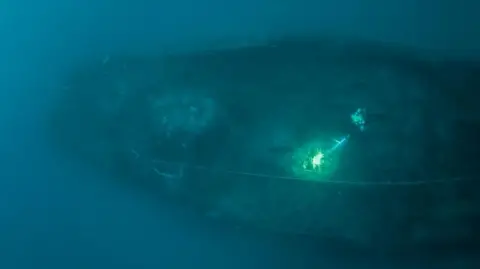 Rick Ayrton Diver and the wreck of the ship from above. Shipwreck and a diver with a torch.