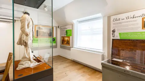 Caroline Bridges Photography An exhibition inside Wirksworth Heritage Centre. There is a glass cabinet on the left with an outfit inside and signs on the wall with information on. 