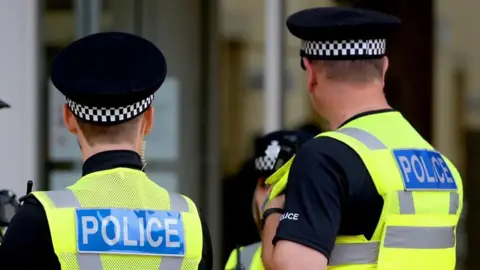 Three police officers in uniform stood outside a blurred glass building in discussion