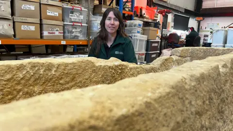 Emma Baugh/BBC Archaeologist sitting behind the stone coffin