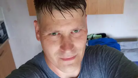 A selfie, looking up and into the camera, he has green eyes and looks like he has wet hair. 