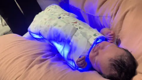 Supplied A baby wrapped in a blanket, which is emitting blue light