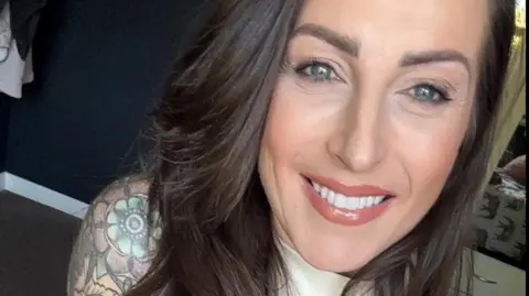 A close up of Kelly Bailey, who has long dark straight hair. You can see a colourful shoulder tattoo on her right arm.