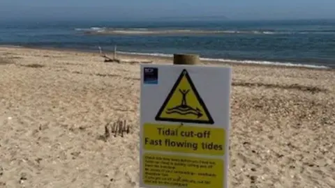 A sandy beach with a warning sign on wooden post and sea behind.
