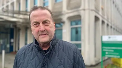 Phil Bialyk wearing a quilted navy blue jacket in front of the Exeter City Council offices
