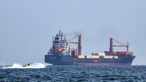 A boat approaches the St Kitt's and Nevis-flagged container ship Marsa Victory while cruising in the waters of the Strait of Hormuz off the coast of Khasab in Oman's northern Musandam peninsula on June 25, 2025.