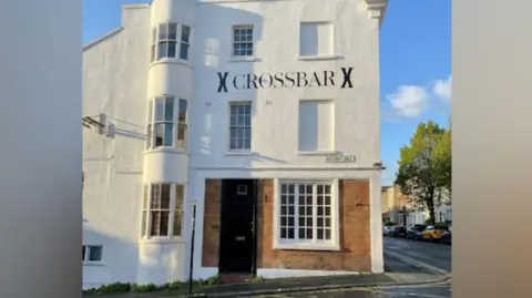 Sally Rawlins A pub which has "X CROSSBAR X" written on the outside. The building is three storeys high and is painted white.