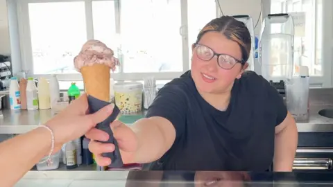 Woman in ice cream shop hands over a cone to a customer