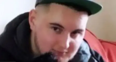 Norfolk Police Joe Dix sits on a red sofa wearing a black baseball cap 