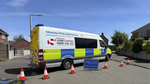 BBC A police van parked across a road with a road closed sign in place