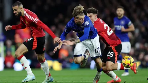 Reuters Jack Clarke, in blue Ipswich Town strip, goes for the ball against Manchester United's Noussair Mazraoui and Manuel Ugarte in red strips.