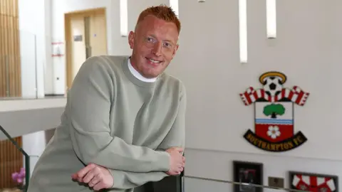 Southampton boss Will Still poses for a photo with the Saints FC badge behind him 