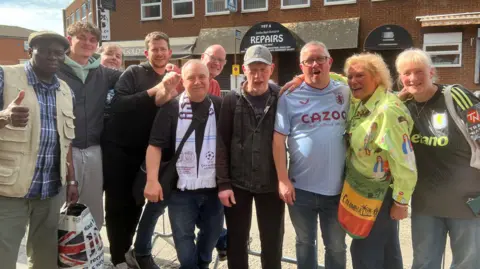 A group of people line up for a photo as they await the Aston Villa parade bus.