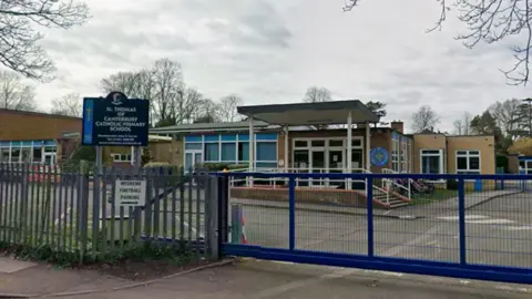 A single-storey primary school behind blue gates, with image taken from the road outside