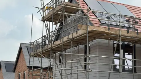 A partially completed new-build house covered in scaffolding, with other modern homes under construction in the background.