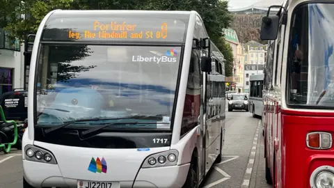 The front of a white bus in Jersey. It is moving and is Liberty Bus.