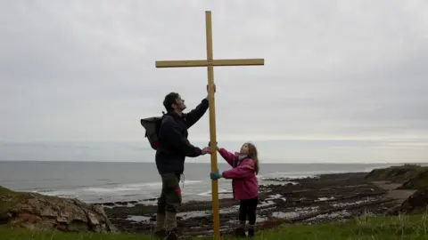 Pete Coppola A photograph from the 1980s with Nadia and Pete Coppola erecting a wooden cross by the sea