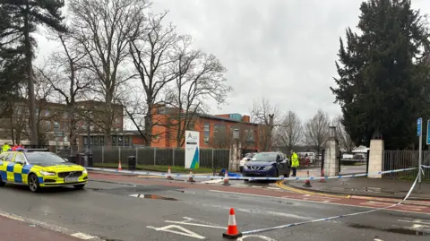 BBC Police standing in the middle of Kings Road, with a police car in front of them and police tape covering the college's entrance.