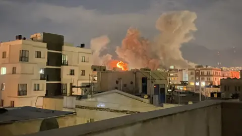 Getty Images A city skyline with flames and smoke in the distance