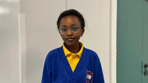 Little girl wearing yellow polo top and blue school uniform cardigan