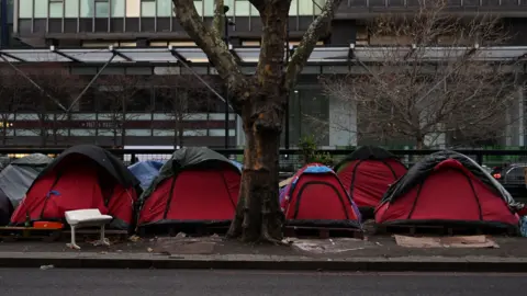 Red tents line a central London street beneath a bare tree. 