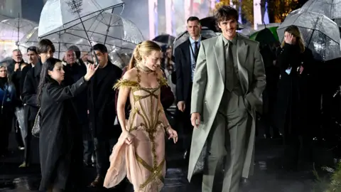 Getty Images Margot Robbie and Jacob Elordi in the rain at the Wuthering Heights premiere. People aroudn them are holding umbrellas for them
