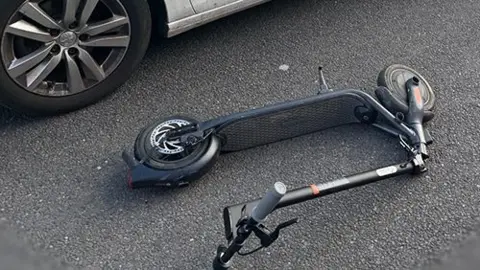 Derbyshire Police An e-scooter lying on the ground next to a police car.