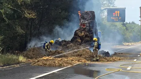 Firefighters tending to a large chunk of hay bales which are still on fire.
