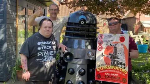 PA Media Three people standing next to a life-size Dalek which was handmade