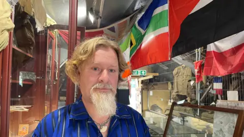 Edd Smith/BBC Paul Smith with flags behind him in Nissan hut museum