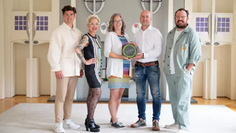 IWC Media The winning couple stand in the middle of judges Danny Campbell, Anna Campbell Jones and Banjo Beale as they are presented with their trophy at the house for an Art Lover.