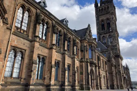 The outside of Glasgow University, a sandstone building with a tower on the right.