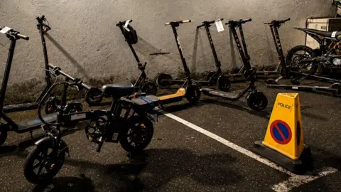 A yellow cone has the word police displayed on it. Electrical bikes are parked next to it. It's night. 