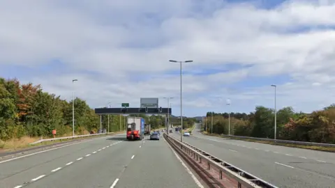 Google maps screengrab of the A55 at Dwygyfylchi, Conwy.  Cars can be seen travelling away from the camera. Blue skies can be seen as green hedges line the road. 
