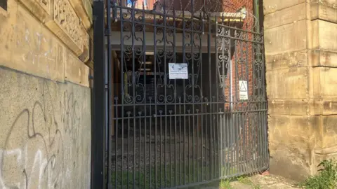 A metal gate in front of a shed with light stone walls on either side