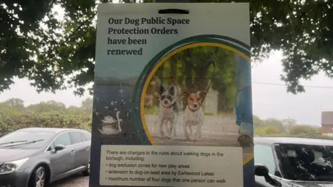 Adrian Harms/BBC A sign which shows two dogs being walked on a lead and states that dog public space protection orders have been renewed along with listing the changes which include the change to limits as well as a dog exclusion zone in new play areas and an extension to a dog-on-lead area.