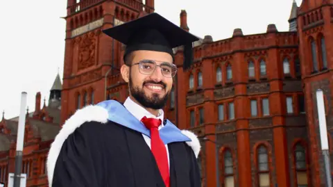 Hamza Al-Huseini Hamza Al-Huseini when he was graduating from the University of Liverpool in 2020. He is standing in his cap and gown outside the red-brick Victoria Building.