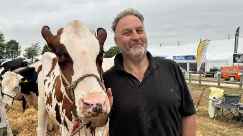 Man wearing a black polo top standing next to a cow at a farm show