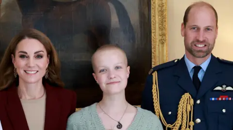 Kensington Palace/Andrew Parsons Liz Hatton, pictured with the Prince and Princess of Wales. The Princess, who is smiling at the camera, wears a burgundy blazer and beige top. She stands next to Ms Hatton, who is wearing a light green jumper and necklace.