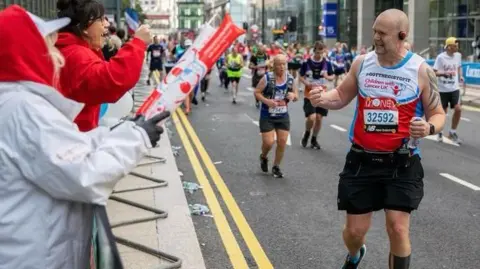 Chris Johnson Chris Johnson is pictured to the right of the image with his fist clenched, smiling at a woman encouraging him during the London Marathon