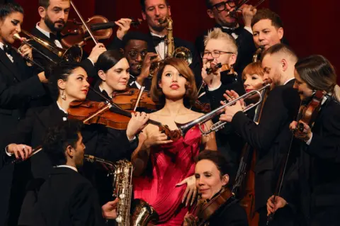 Aliyah Otchere Raye in a red dress, surrounded by orchestral musicians