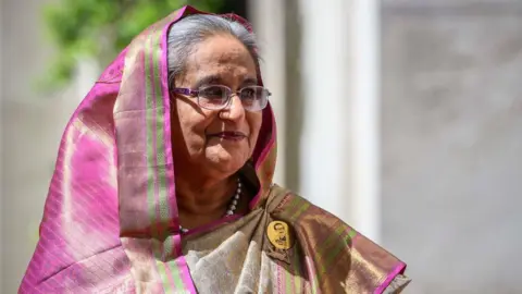 Getty Images Sheikh Hasina is pictured looking to her left slightly smiling, in a pink and green head dress. 