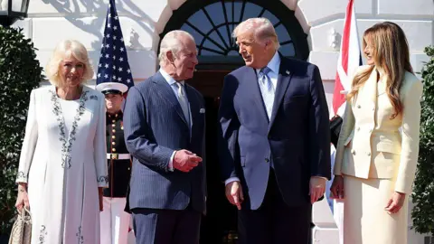 Queen Camilla, King Charles, President Donald Trump and First Lady Melania Trump stand in line, with the King and Trump conversing, while Melania smiles at the two. 