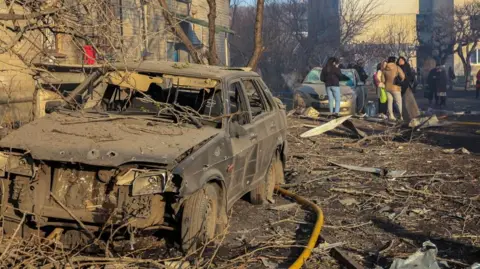 EPA A burned out car in the foreground, next to some damaged buildings