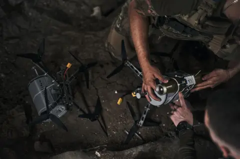Getty Images An arm holds a silver drone on the floor in the dark