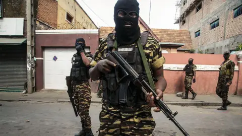 AFP a través de Getty Pictures de un hombre en Fatgu Un esquí negro y esquí negro contiene el rifle automático sobre el cofre.