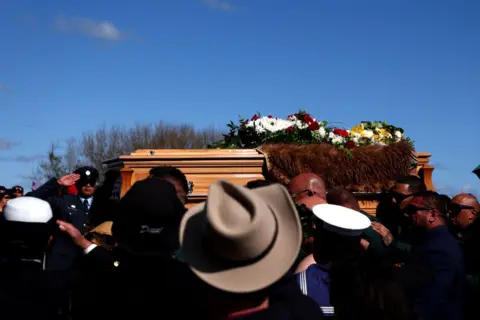 Getty Images Onlookers watch and salute a coffin draped in furs being carried by pall bearers